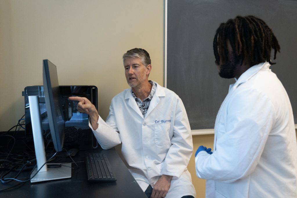 An instructor indicating something on a computer monitor to a student.