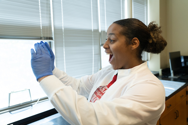 Student in lab coat excitedly examining a petri dish.