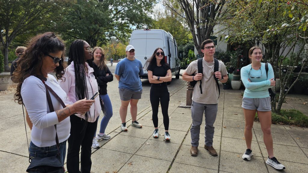 Eight students on a sidewalk, waiting to enter a destination.