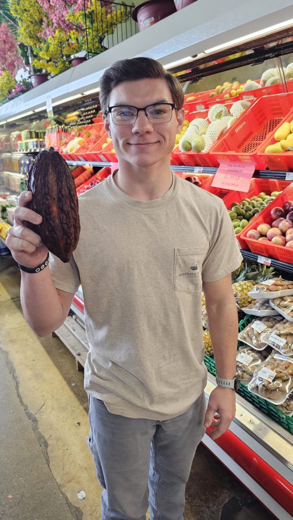 Student holding an Asian fruit in the aisle of a grocery store.