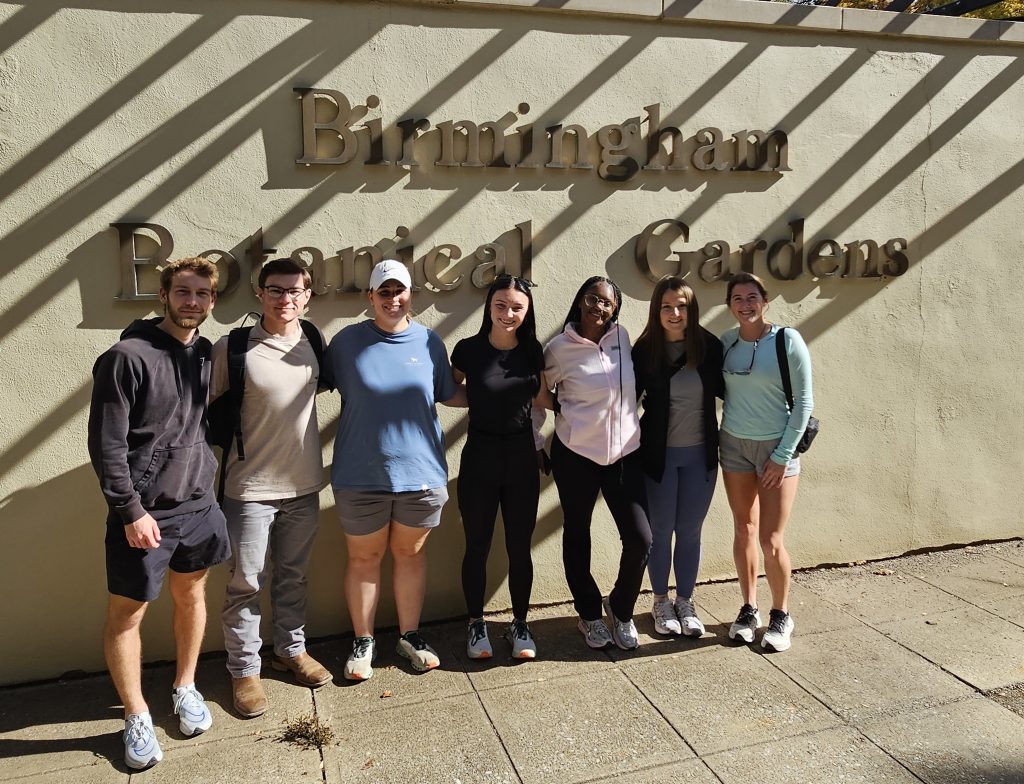 Botany students standing in front of wall with a Birmingham Botanical Garden sign.